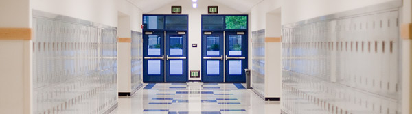 A well-lit school hallway with lockers lining the walls and double doors at the end.