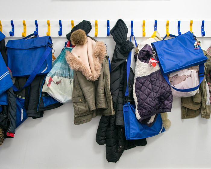 A row of colorful bags and coats hanging on wall-mounted hooks.