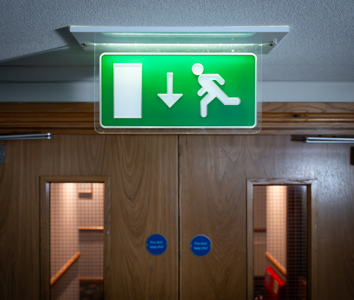 A lit fire exit sign above a wooden fire door